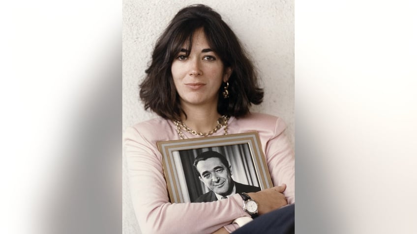 Ghislaine Maxwell wearing a pink sweater and holding a black and white portrait of her father in a frame.