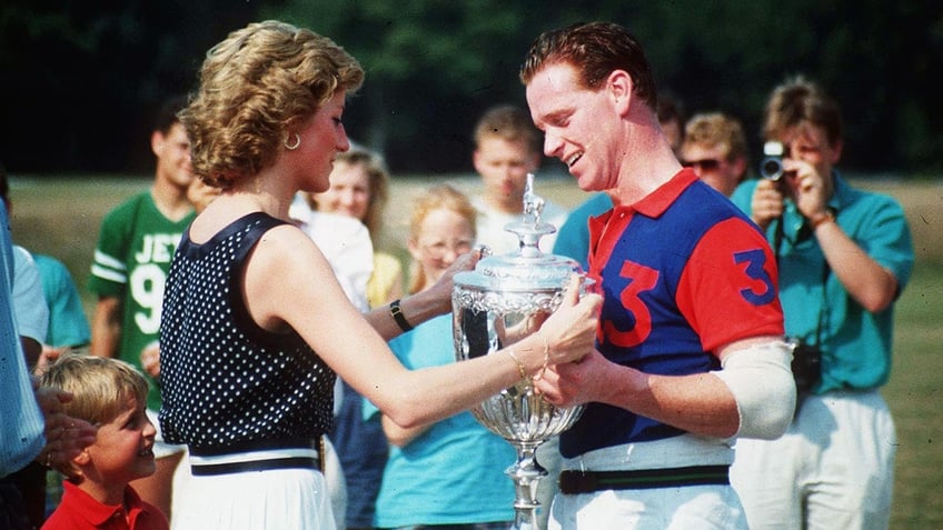 Princess Diana in a sleeveless black polka dot blouse and white pants handing a polo prize to James Hewitt