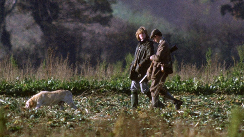 Princess Diana walking with Prince Charles in a field with a dog.