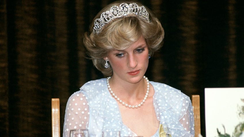 Princess Diana wearing a pale lace dress and a tiara with pearls looking down.