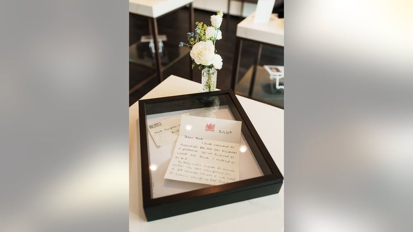 A letter written by Princess Diana is framed next to white flowers in a crystal vase.