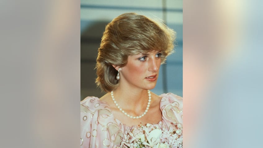 A close-up of Princess Diana in a pale pink dress holding flowers.