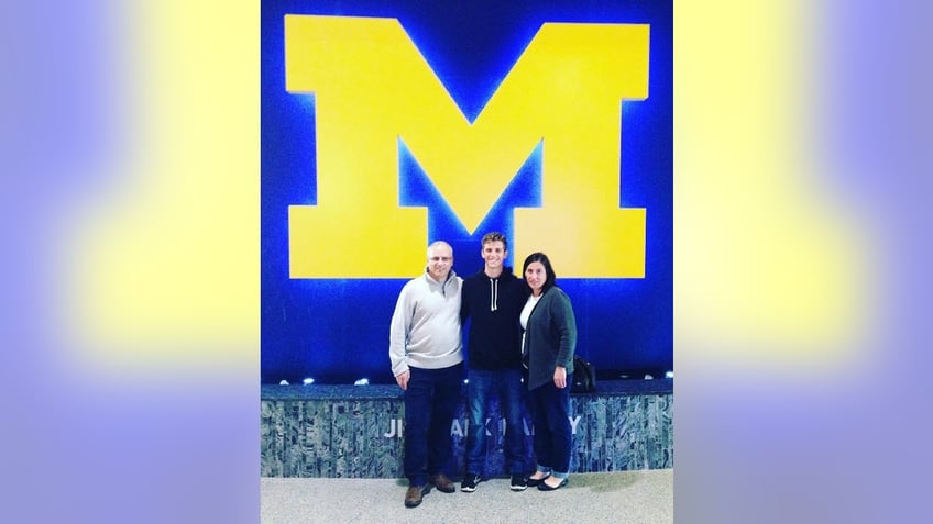 Joseph Hertgens poses with his parents beneath a University of Michigan sign