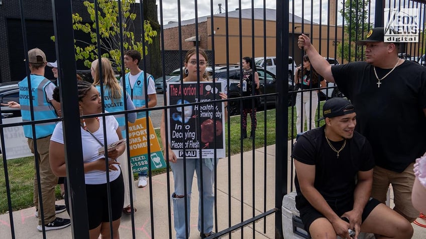 Protestors behind a fence hold up signs