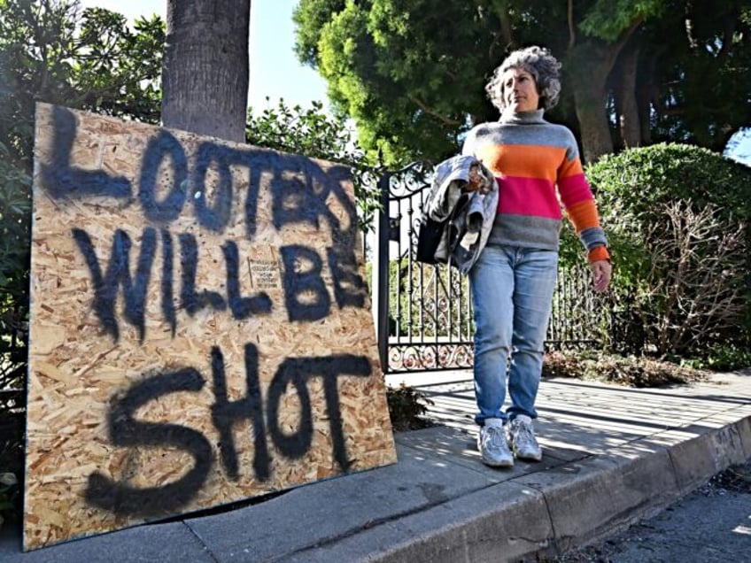 An Altadena resident walks past a sign in front of her home on January 13, 2025 warning lo