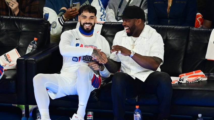 two men seated courtside at NBA game shaking hands, laughing