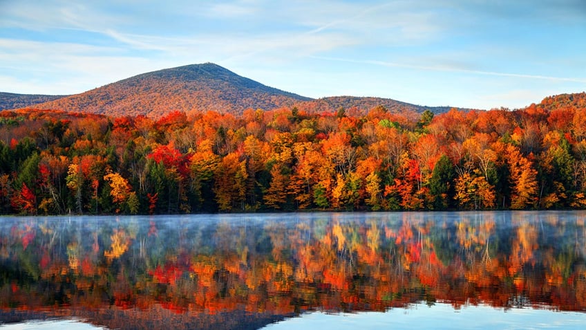 Early morning autumn light near Killington, Vermont, showing many trees in different colors reflecting on the lake.