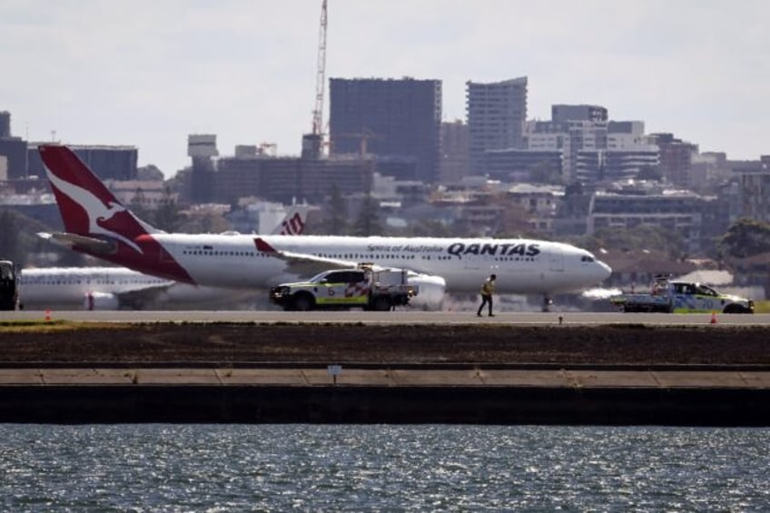 Workers check the runway as a Qantas plane prepares to take off behind them at Sydney Airp