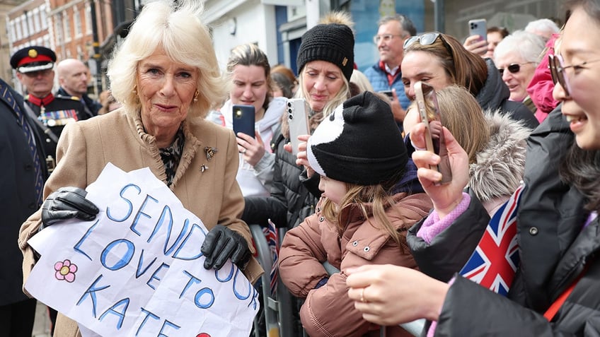 A photo of Queen Camilla holding a sign that reads "sending our love to Kate"
