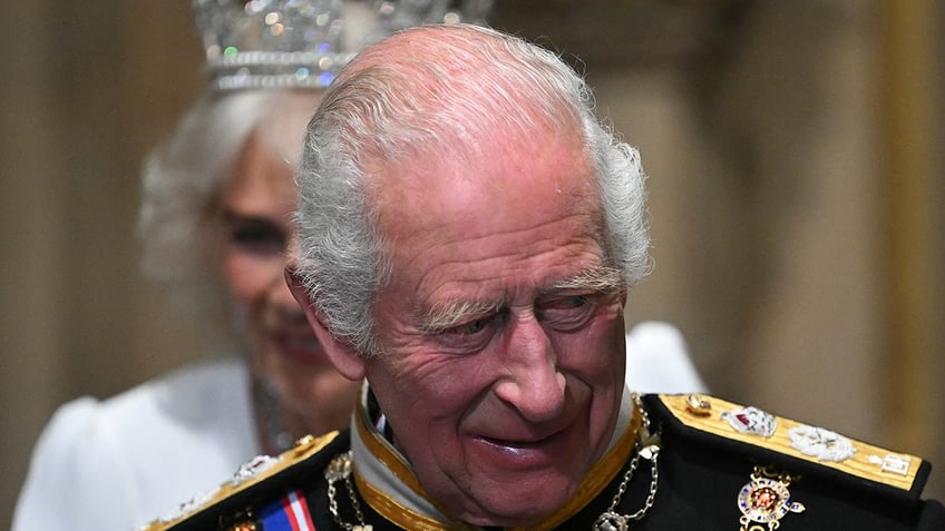 A close-up of King Charles looking down in a royal uniform and smiling.