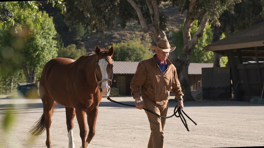 Monty Roberts walking with a brown horse.