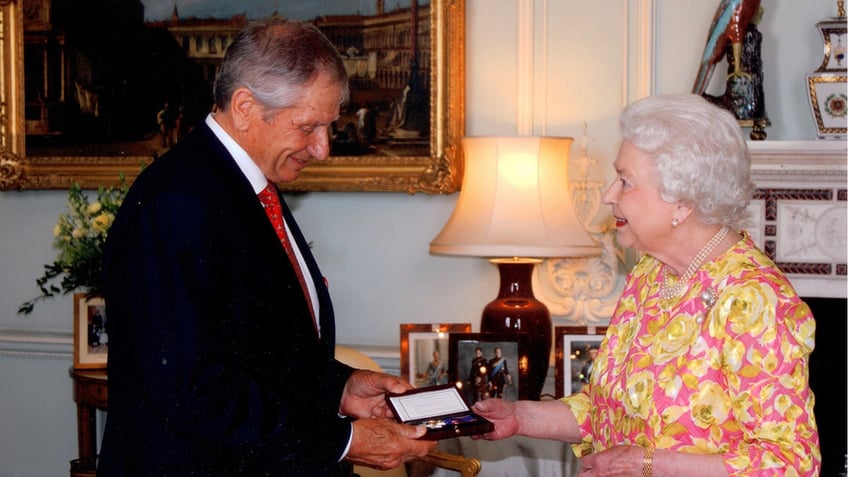 Queen Elizabeth wearing a floral dress handling a medal to Monty Roberts in a suit.