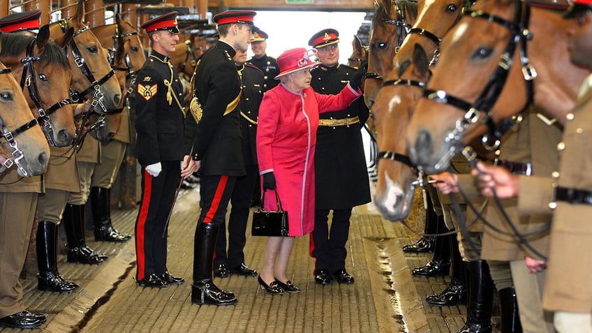 Queen Elizabeth wearing a hot pink coat surrounded by guards and brown horses.