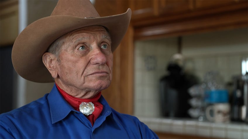 Monty Roberts in a blue shirt and brown cowboy hat looking up.