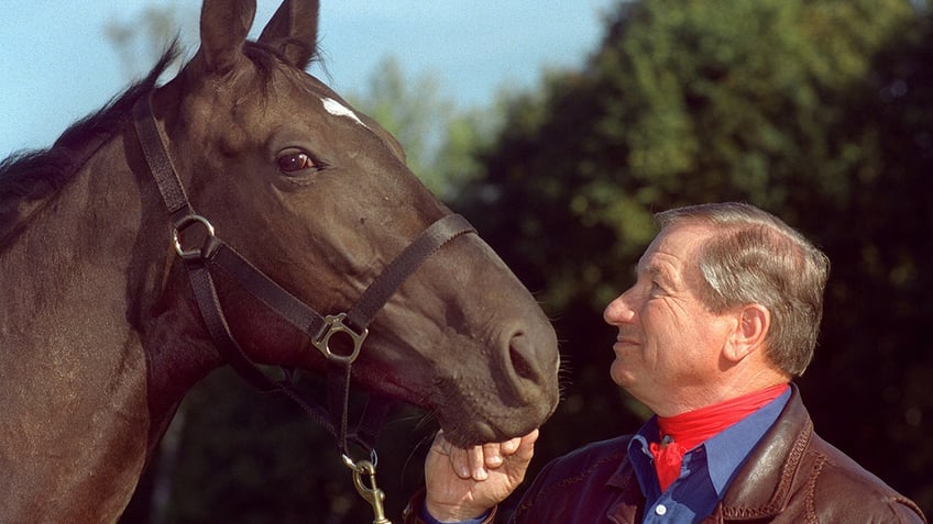 Monty Roberts looking at a brown horse.