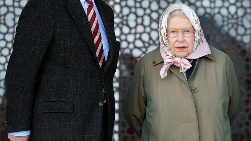 Queen Elizabeth wearing a coat and a scar wrapped around her head standing