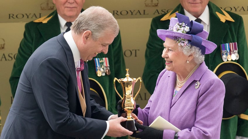 Queen Elizabeth wearing a purple coat dress and matching hat handing Prince Andrew an award.