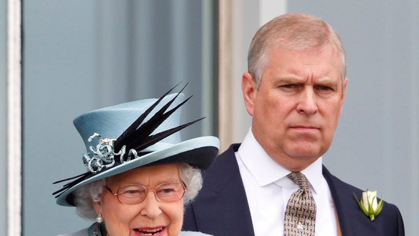 Queen Elizabeth in a blue coatdress and matching hat standing next to Prince Andrew looking sternly in a suit.