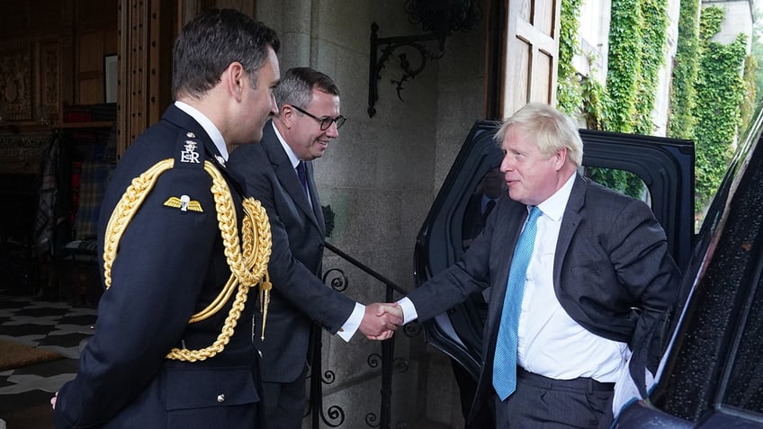 Boris Johnson in a suit and bright blue tie shakes hands with Equerry Lieutenant Colonel Tom White and her private Secretary Sir Edward Young ahead of his visit with the Queen