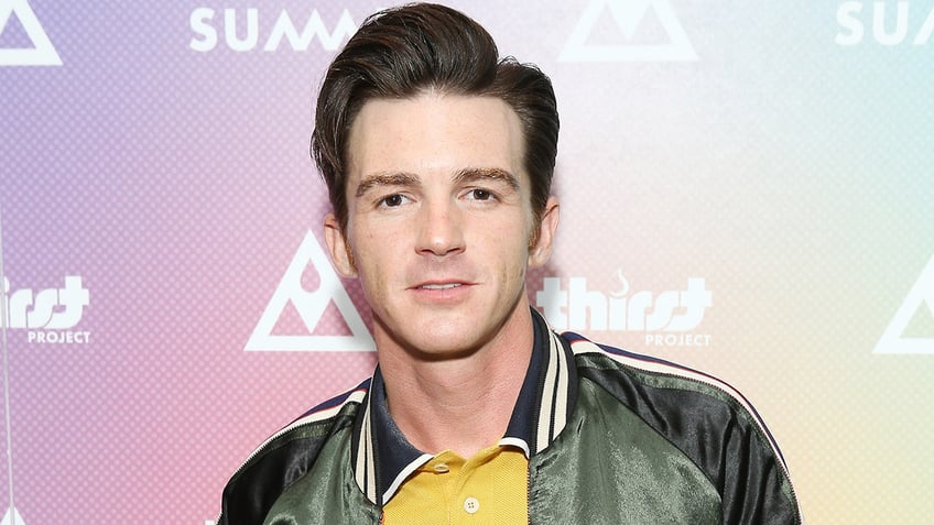 Drake Bell wears a green jacket and yellow under shirt with a blue striped collar on the red carpet