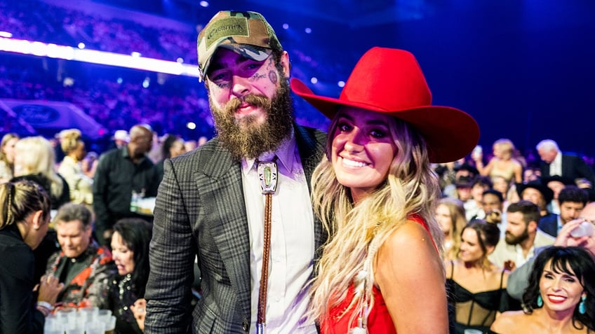 Lainey Wilson sports red cowboy hat next to Post Malone.