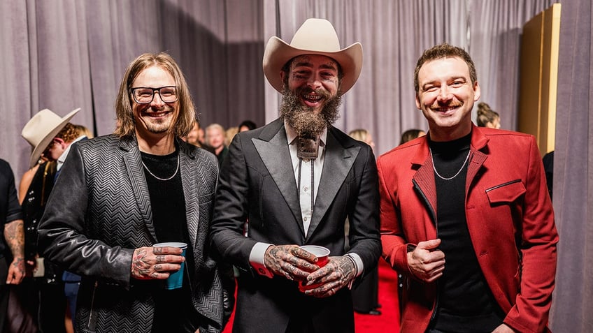 Post Malone smiles alongside Morgan Wallen and HARDY at country music awards.