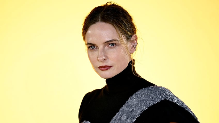 Rebecca Ferguson looks serious on the carpet in a black turtleneck dress with a sparkly sash