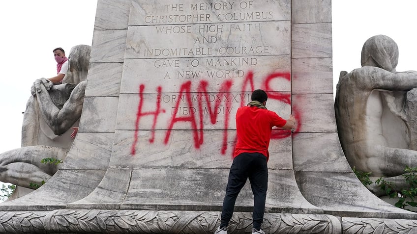 man spraypainting "Hamas" on a statue