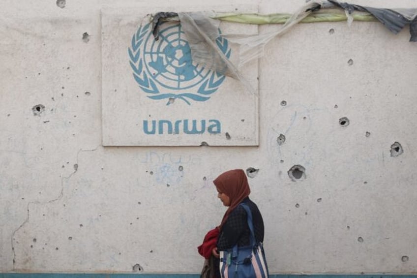 A Palestinian woman walks past a damaged wall bearing the UNRWA logo at a camp for interna