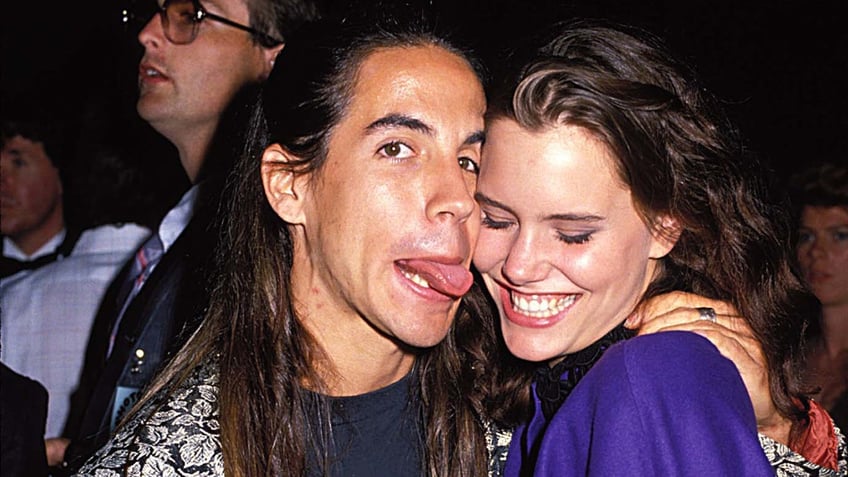 A close-up of Anthony Kiedis sticking his tongue out at Ione Skye's face as she smiles.