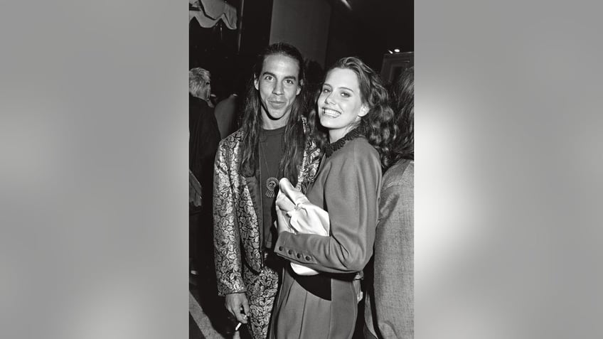 A black and white photo of Anthony Kiedis and Ione Skye posing together as Ione Skye smiles.