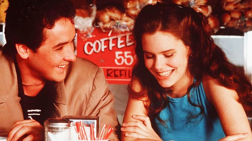 John Cusack smiling at Ione Skye who looks down grinning in a scene from Say Anything.