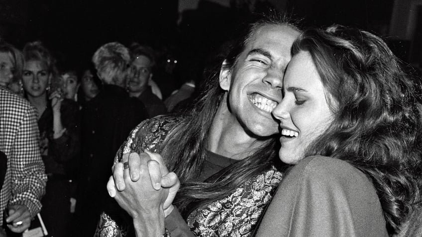 Anthony Kiedis smiling against Ione Skye as they hold hands.