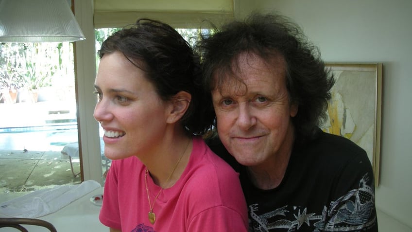 Ione Skye wearing a pink shirt sitting next to Donovan who is looking at the camera.