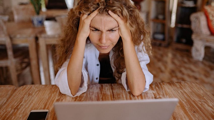 Woman sitting at a table, staring at her laptop in an upset manner.