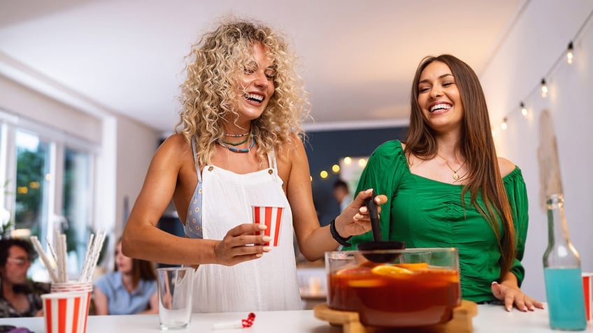 Two women around a punch bowl at a party.