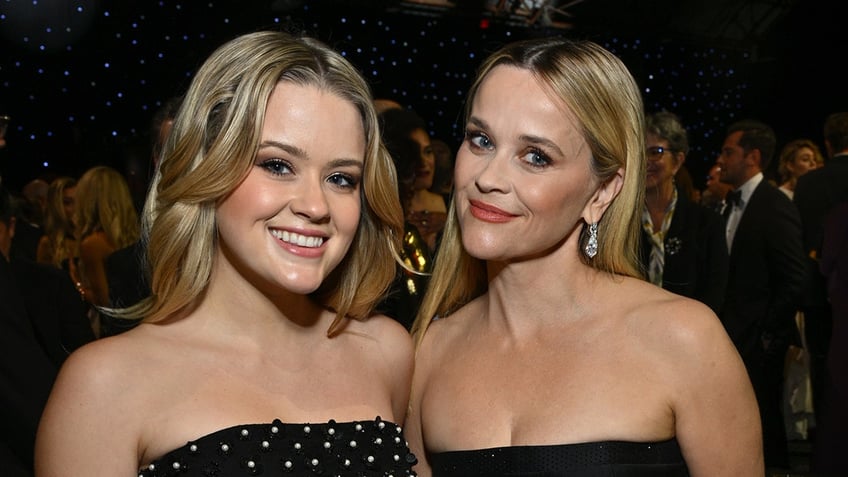 Ava Phillippe in a polka dot dress smiles next to mother Reese Witherspoon in a black dress