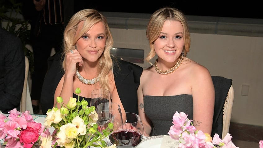 Reese Witherspoon sits at a table with daughter Ava Phillippe who smiles for the camera