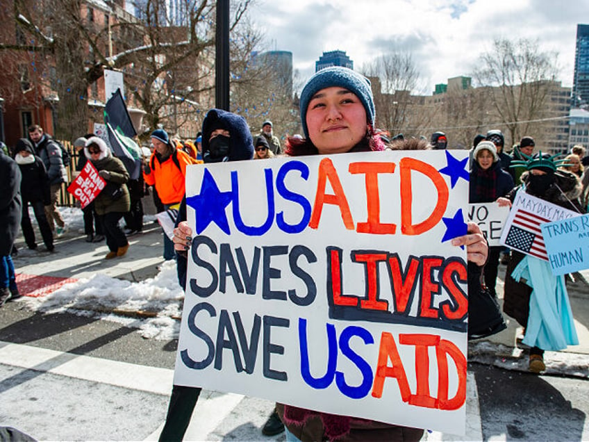 A woman holds a sign supporting USAID as demonstrators rally against US President Donald T