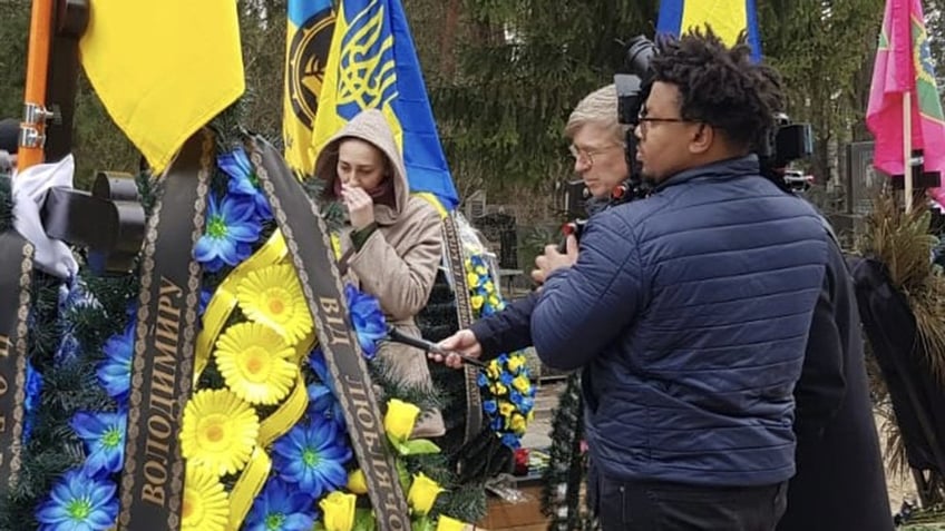 Fox News' Greg Palkot standing with camera man and woman by cemetery in Kyiv