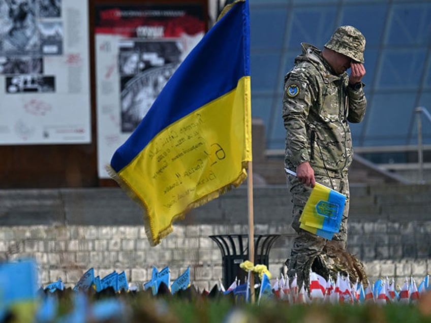 A serviceman mourns next to a Ukrainian flag at a makeshift memorial for fallen soldiers a