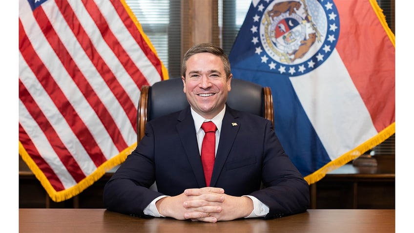 Andrew Bailey, Missouri AG, at desk with flags behind him