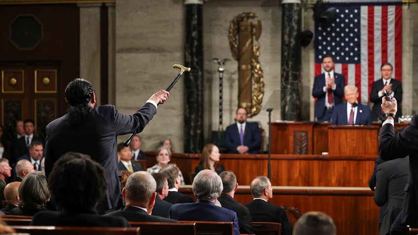 Rep. Al Green seen from behind, shaking cane at Trump on dais