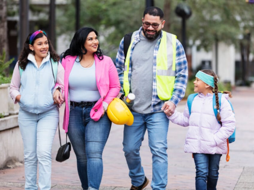 An Hispanic family on their way to school and work, walking together in the city, holding
