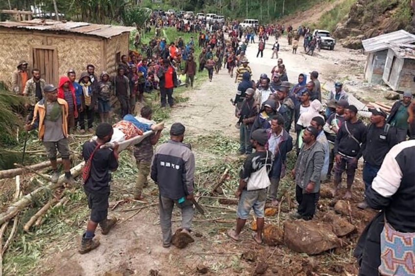 Locals carry a person on a stretcher from the site of a landslide in Papua New Guinea's En