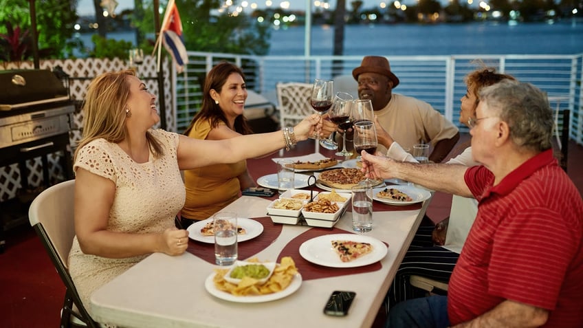 Five friends raise their wine glasses and bring them together for a toast while dining along the waterfront.