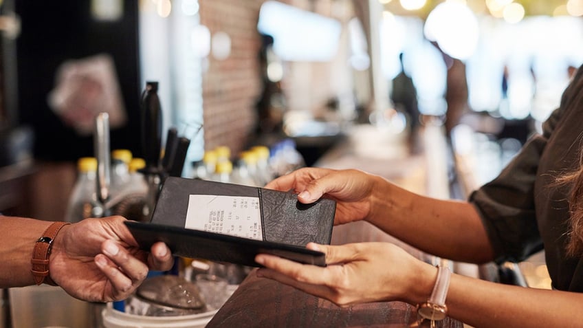 Woman's hands seen holding out a restaurant bill in a holder as server takes it