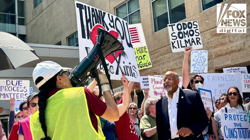 Demonstrators rally outside a courthouse holding signs in support of Kilmar Garcia and due process rights. A woman uses a megaphone while others raise signs reading 