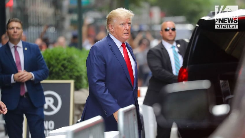 Donald Trump wearing a red tie and blue suit walking on the streets of New York City