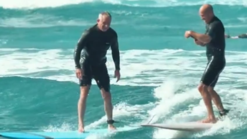 RFK Jr and Kelly Slater standing on surfbaords in the ocean